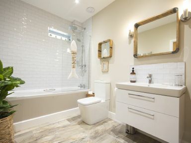A bathroom with a bathtub shower and toilet next to a sink with mirror at Marmalade Cottage in Seahouses