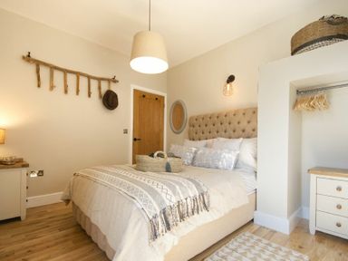 A bedroom with a bed a bedside table a wooden coat rack a wooden door and an open wardrobe at Marmalade Cottage in Seahouses