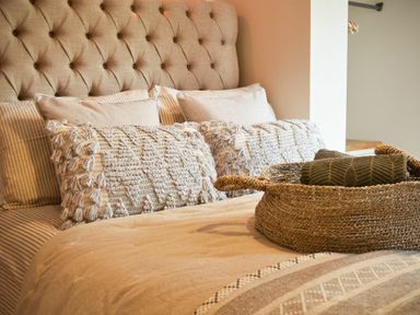 A bed with a beige tufted headboard pillows and a woven basket with rolled towels at Marmalade Cottage in Seahouses