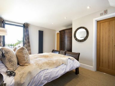 A bedroom with a bed pillows and blanket a wooden wardrobe a round mirror and a wooden door at Marmalade Cottage in Seahouses