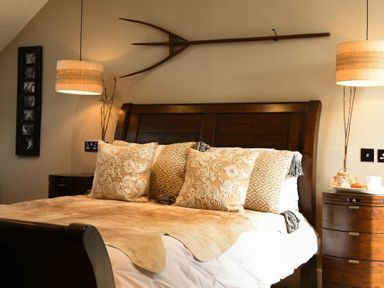 A bedroom with a wooden bed with patterned pillows and animal hide bed cover at Marmalade Cottage in Seahouses