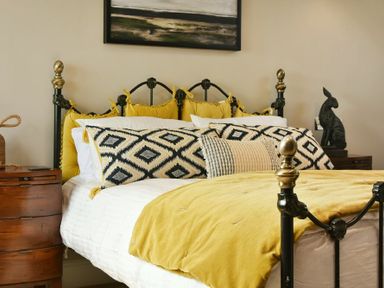 A bed with yellow pillows and a yellow blanket a wooden nightstand with a rope handle and a sculpture on another nightstand at Marmalade Cottage in Seahouses