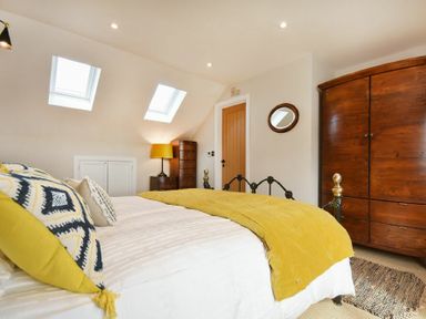 A bedroom with a bed made with yellow and patterned pillows a wooden wardrobe a dresser and two skylight windows at Marmalade Cottage in Seahouses