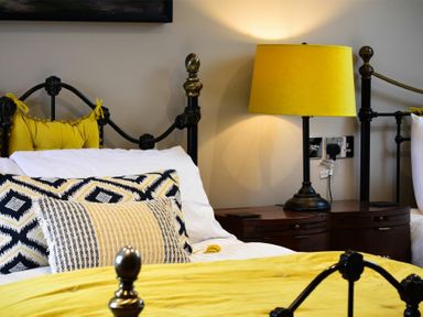 A bedroom with yellow bedding yellow lamp on bedside table and metal bed frame at Marmalade Cottage in Seahouses