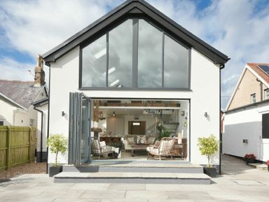 A two-story house with large glass windows and open folding doors leading to a living room at Marmalade Cottage in Seahouses