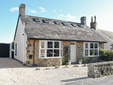 A stone cottage with windows and front door and gravel driveway at Marmalade Cottage in Seahouses
