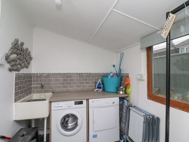 A laundry room with a washing machine and dryer under a countertop a sink and various cleaning supplies at Anchor Cottage Seahouses
