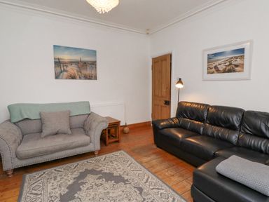 A living room with two sofas a floor lamp wooden door and framed pictures on white walls at Anchor Cottage Seahouses