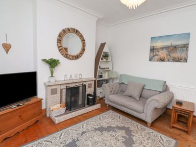 A living room with a fireplace a gray sofa a television and a decorative mirror at Anchor Cottage (Seahouses) in Seahouses