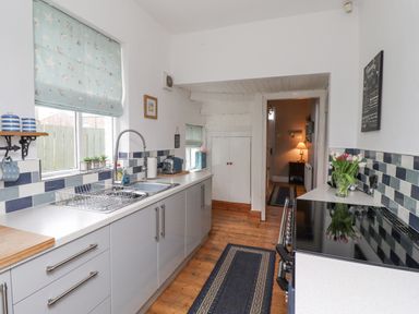 A kitchen with a sink, stove, countertop, cabinets, and blue patterned window blinds at Anchor Cottage in Seahouses