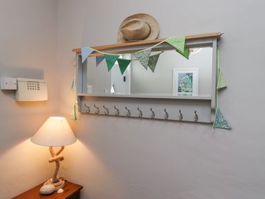 A wall-mounted mirror with hooks and colorful bunting above a wooden table with a lamp and stones at Anchor Cottage Seahouses