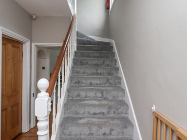 A staircase with grey carpet and wooden handrail next to a wooden door at Anchor Cottage Seahouses