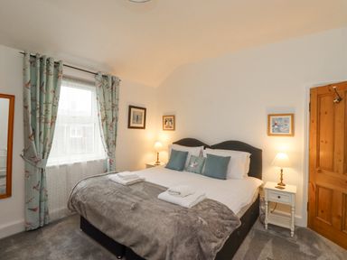 A bedroom with a bed with pillows and folded towels beside windows with curtains at Anchor Cottage (Seahouses) in Seahouses