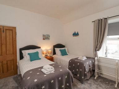 A bedroom with two single beds with star blankets and teal pillows at Anchor Cottage Seahouses