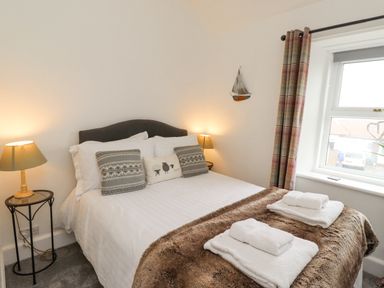 A bedroom with a bed lamps bedside tables window and folded towels at Anchor Cottage (Seahouses) in Seahouses