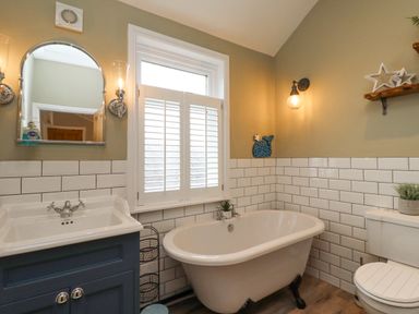A bathroom with a bathtub sink toilet mirror and window at Anchor Cottage Seahouses