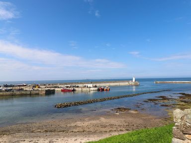 A harbor with boats docked near a pier and a lighthouse by the sea at Anchor Cottage Seahouses