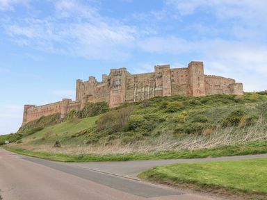 A large stone castle on a hill with grass and bushes at Anchor Cottage in Seahouses