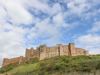 A large stone castle on top of a grassy hill under a partly cloudy sky