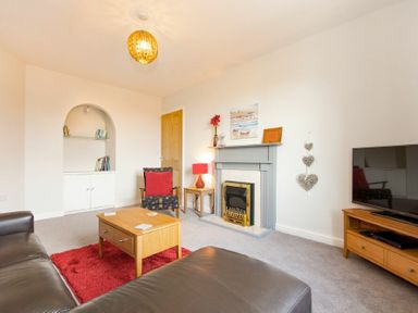 A living room with a fireplace a wooden coffee table a TV on a stand and armchairs at Church View in Bamburgh