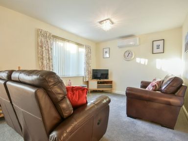 A living room with leather sofas a TV on a wooden stand a wall clock and framed pictures at Annstead House in Seahouses