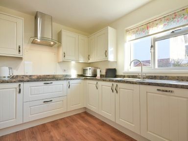 A kitchen with white cabinets a stainless steel oven hood a microwave sink under a window and a wooden floor at Annstead House in Seahouses