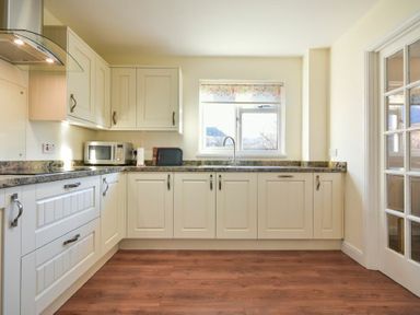 A kitchen with white cabinets wooden floor a window a microwave oven and a sink at Annstead House in Seahouses
