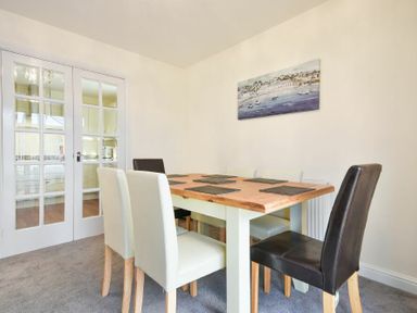 A dining room with a wooden table and six chairs near glass double doors at Annstead House in Seahouses