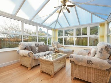 A conservatory with wicker sofas chairs and a glass coffee table at Annstead House in Seahouses