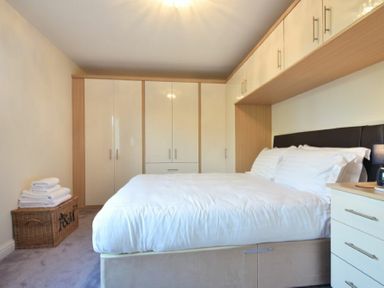 A bedroom with a bed white bedding built in wardrobes and a basket with towels at Annstead House in Seahouses