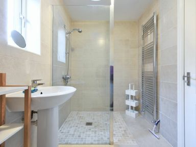 A bathroom with a shower area with glass partition a pedestal sink a heated towel rail and a window at Annstead House in Seahouses