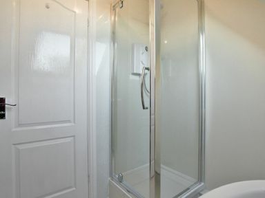 A bathroom with a white door and a shower enclosure with glass doors at Annstead House in Seahouses