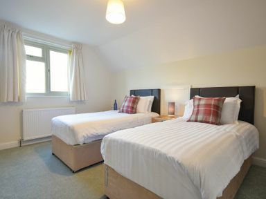 A bedroom with two single beds a nightstand with a lamp between the beds and a window with curtains at Annstead House in Seahouses
