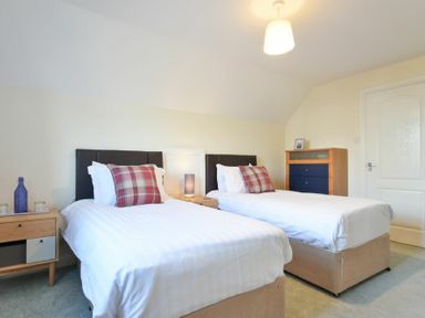 A bedroom with two single beds with checked pillows a wooden nightstand a lamp and a dresser at Annstead House in Seahouses