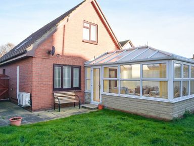A brick house with a glass conservatory and a wooden bench in a garden at Annstead House in Seahouses