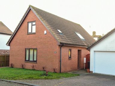 A brick house with brown roof and windows next to a white garage with a closed door at Annstead House in Seahouses