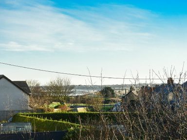 A suburban neighborhood with houses trees and a view of fields under a blue sky at Annstead House in Seahouses