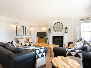 A living room with black leather sofas a wooden coffee table a fireplace with a round mirror and two lanterns at Cargoes in Craster