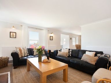 A living room with black sofas a wooden coffee table with flowers and food at Cargoes in Craster