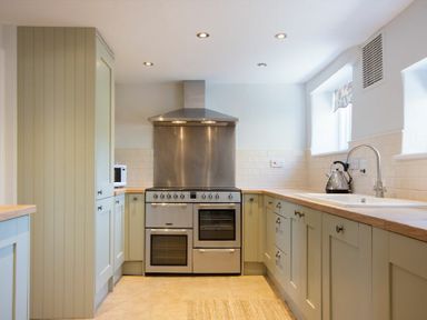 A kitchen with a stainless steel oven and stove a kettle on the counter and light-colored cabinets at Cargoes in Craster