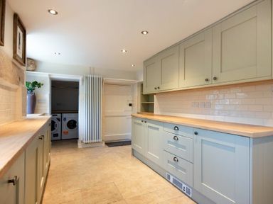 A kitchen with cabinets and wooden countertops and a laundry room with washer and dryer visible at Cargoes in Craster