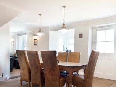 A dining room with a wooden table and six brown chairs at Cargoes in Craster