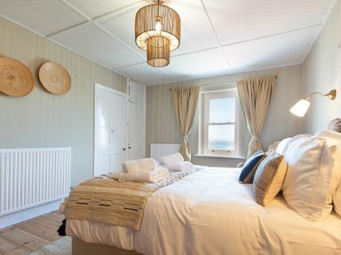 A bedroom with a bed with pillows and towels near a window with curtains at Cargoes in Craster