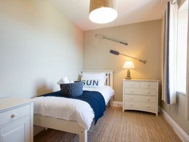 A bedroom with a single bed a nightstand a chest of drawers and two decorative oars on the wall at Cargoes in Craster