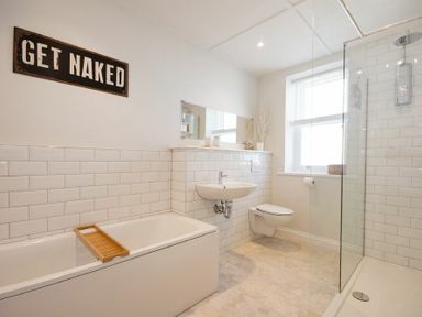 A bathroom with a bathtub a wall-mounted sink toilet and walk-in shower at Cargoes in Craster