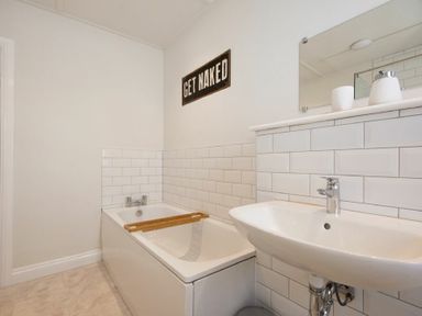 A bathroom with a bathtub sink mirror tiled walls and a wooden bath tray at Cargoes in Craster