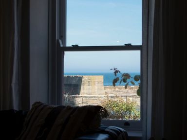 A window with a view of a stone wall sea and blue sky with plants in the foreground at Cargoes in Craster
