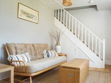 A living room with a wooden sofa and cushions a wooden chest coffee table a staircase and a large vase with branches at Cargoes in Craster