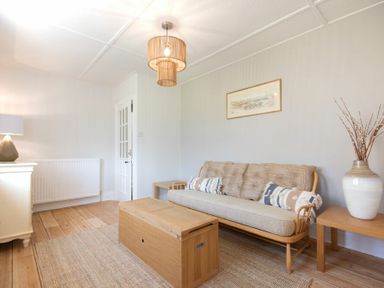 A living room with a wooden sofa with cushions a wooden table a rug and a vase with branches at Cargoes in Craster