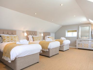 A bedroom with three single beds and a large mirror above a dresser at Cargoes Craster